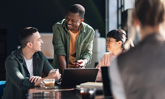Three young professionals look at a laptop together