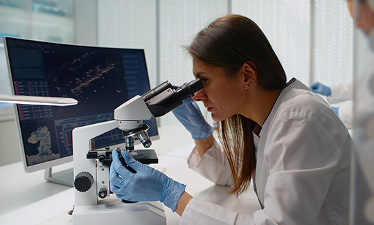 A health care professional looks through a microscope.
