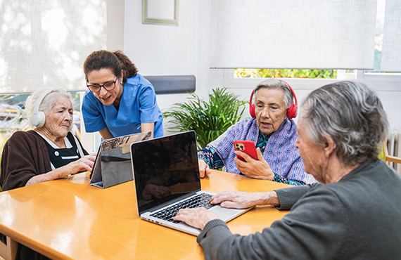 A health care worker assists older adults using laptops.