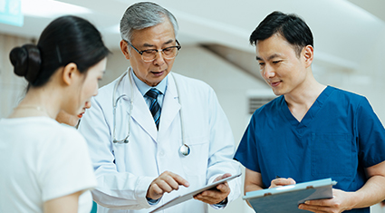 Three medical professionals having a discussion while studying clipboards