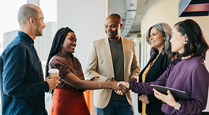 A group of diverse professionals shake hands together over a proposal.