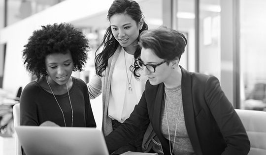 Three professional women look at a laptop together