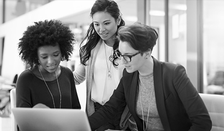 Three professional women look at a laptop together