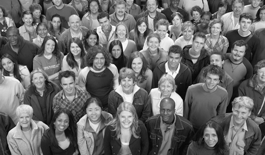 A large diverse crowd stands together, smiling