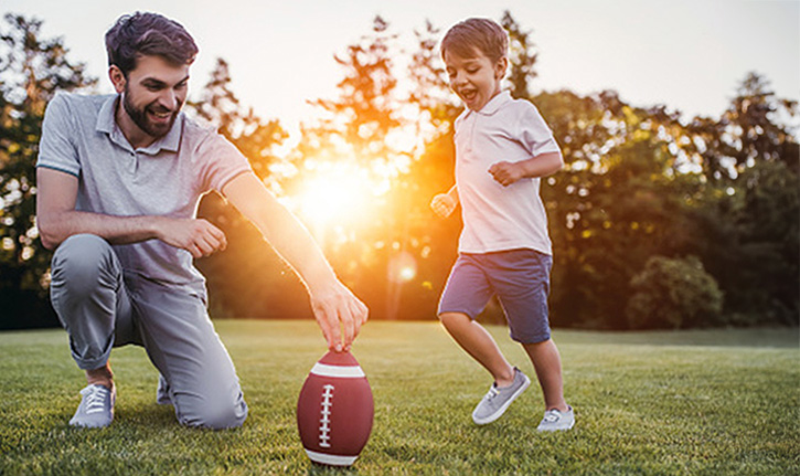 Father and son playing football outside in the yard.
