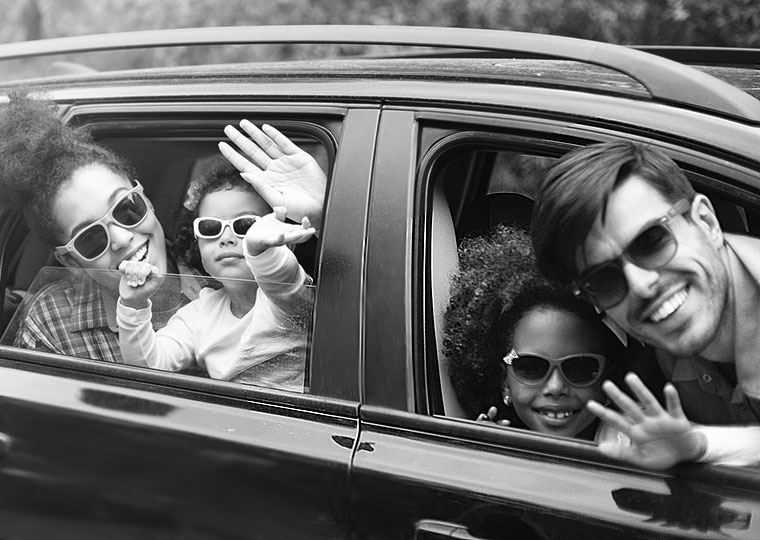 A family smiles and waves from their car windows. 