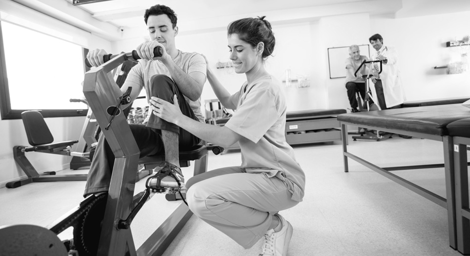 A medical professional helps a man on a stationary bicycle