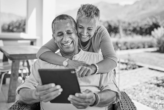 A man and woman smile while looking at a tablet screen together.