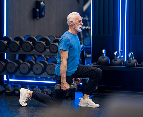 A senior man lifts weights at the gym.