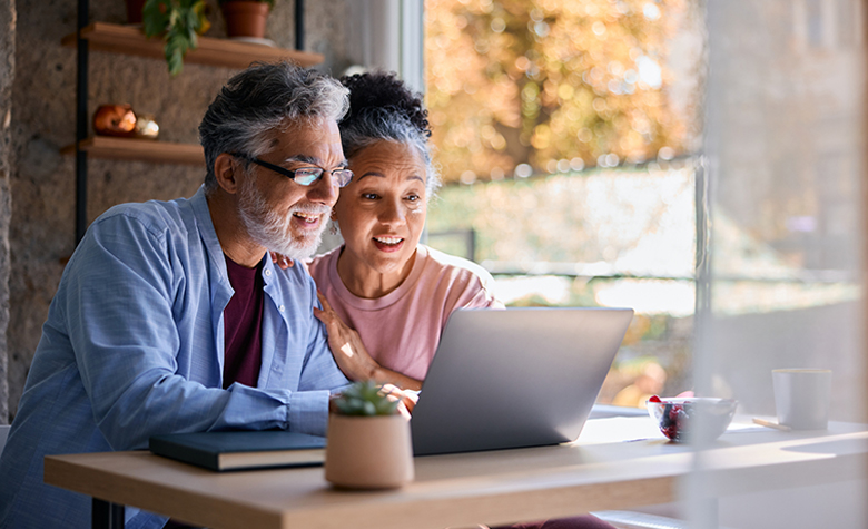 A couple smiles while looking at a laptop screen.