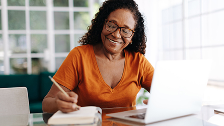 A woman takes notes next to her laptop.