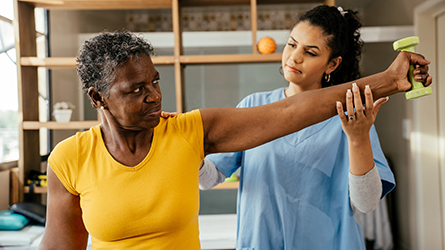 A physical therapist helps a woman move her arm
