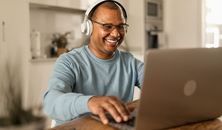 A man wearing headphones smiles at his laptop.