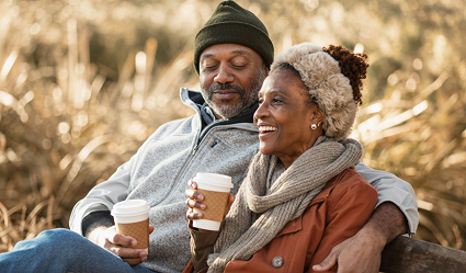 A woman and man snuggle up outside in cold weather while drinking hot coffee.