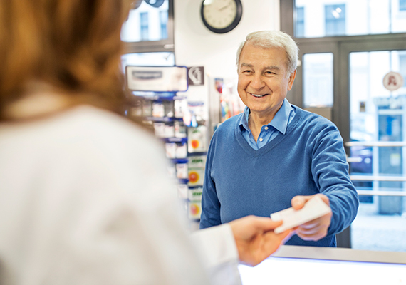 An older man with a Medicare plan hands his prescription to his pharmacist.