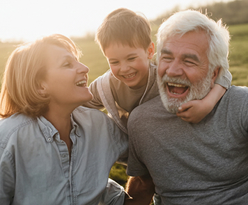 An older couple sits smiling, with a smiling grandchild between them