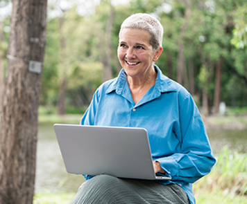 An older woman sitting outside with a laptop in her lap