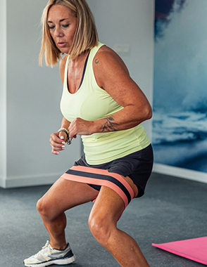 A senior woman uses a band to do a lower body work out.