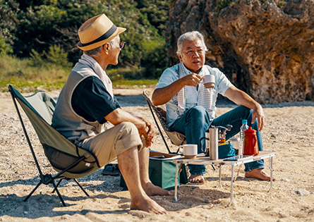 Two older men sit together on the beach while camping.