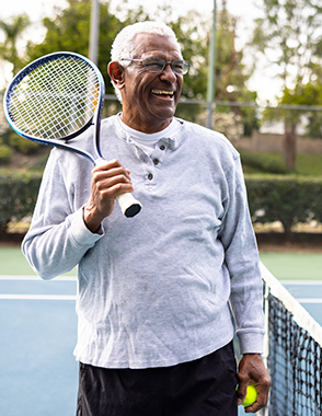 A senior man laughs while playing tennis.