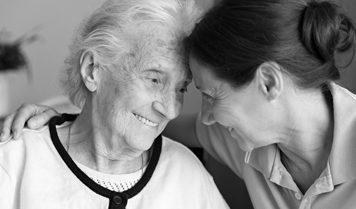 Two women smile while embracing each other with their foreheads pressed together.