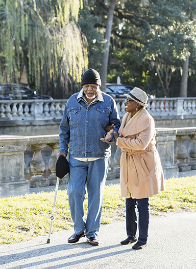 An older woman walks arm in arm with an older man with a cane.