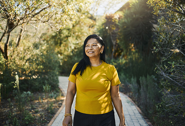 An older woman smiles as she walks down a tree-lined path.