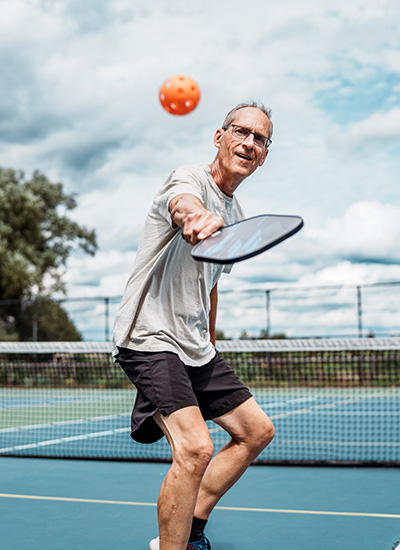 An older man plays pickleball on an outdoor court.