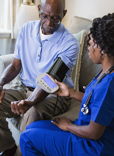 A female nurse checks the blood pressure of an older gentleman during a checkup as they discuss aging in place.
