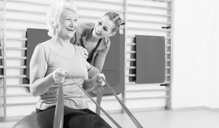 A woman exercises with resistance bands and the help of a trainer.