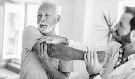 A man stretches his arm with the help of a Medicare doctor. 