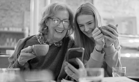 Two women smile while looking at a phone together.