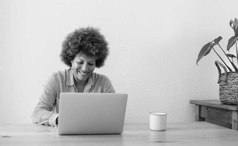A woman smiles while looking at her laptop screen.