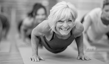 A woman smiles while doing pushups in a fitness class. 