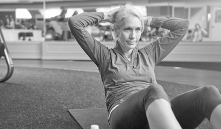 A senior woman completes a sit-up in a gym.