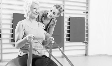 A physical therapist helps a woman use resistance bands for therapy.