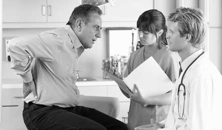 A man with a backache speaks to a man and woman in the professional medical field.