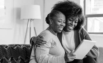 A mother and daughter embrace while looking at a tablet.