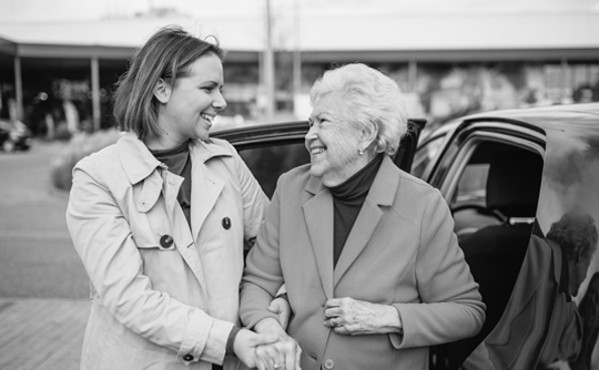 A caregiver holds hands with her loved one as they get out of a car.