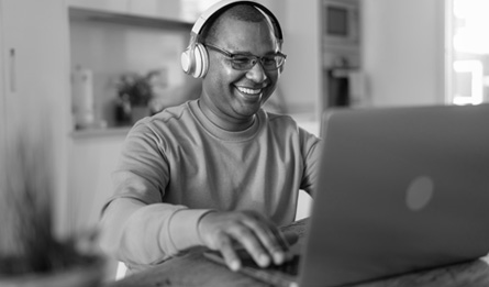 A man wearing headphones smiles at his laptop.