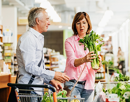 An older man and woman look at some celery in a grocery store.