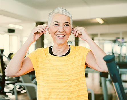 A senior woman puts headphones in her ears while working out at a gym.