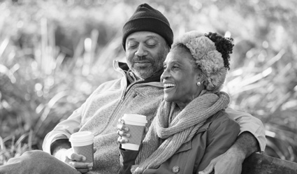 A woman and man snuggle up outside in cold weather while drinking hot coffee.