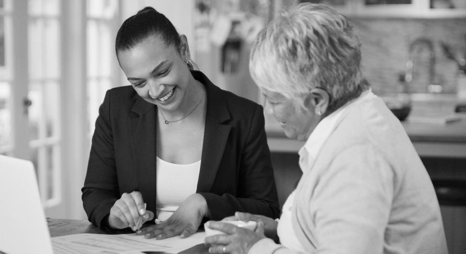 Two women sit at a table reviewing paperwork together