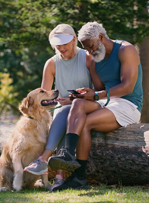 A senior couple takes a break from a walk to look at their smartphones.