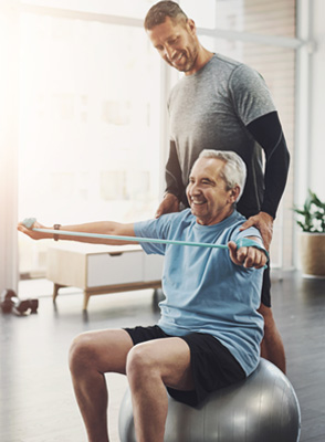 A senior man completes a physical therapy exercise with a phyiscal therapist supervising him.