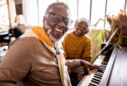 A senior man and woman play piano together.