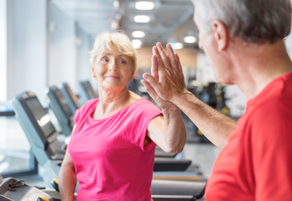 A senior woman high fives an older man during a workout at the gym.