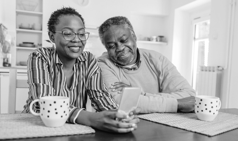 A man and woman sit closely together while looking at a smartphone.