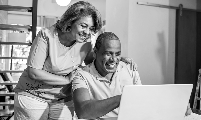 A man and woman smile while looking at a laptop screen together